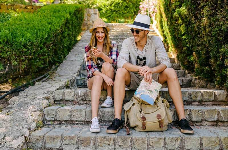 Couple planning travel route with map while sitting on stone stairs outdoors